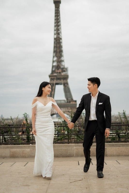 Suthida and Thanapat walking hand in hand by the Eiffel Tower